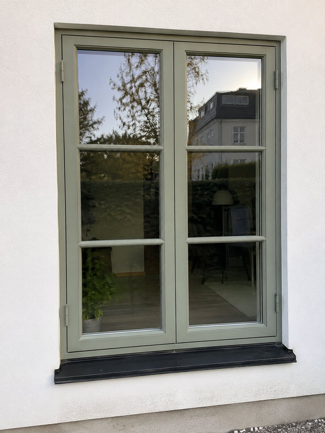 Grönmålat spröjsat träfönster i putsad fasad efter renovering
